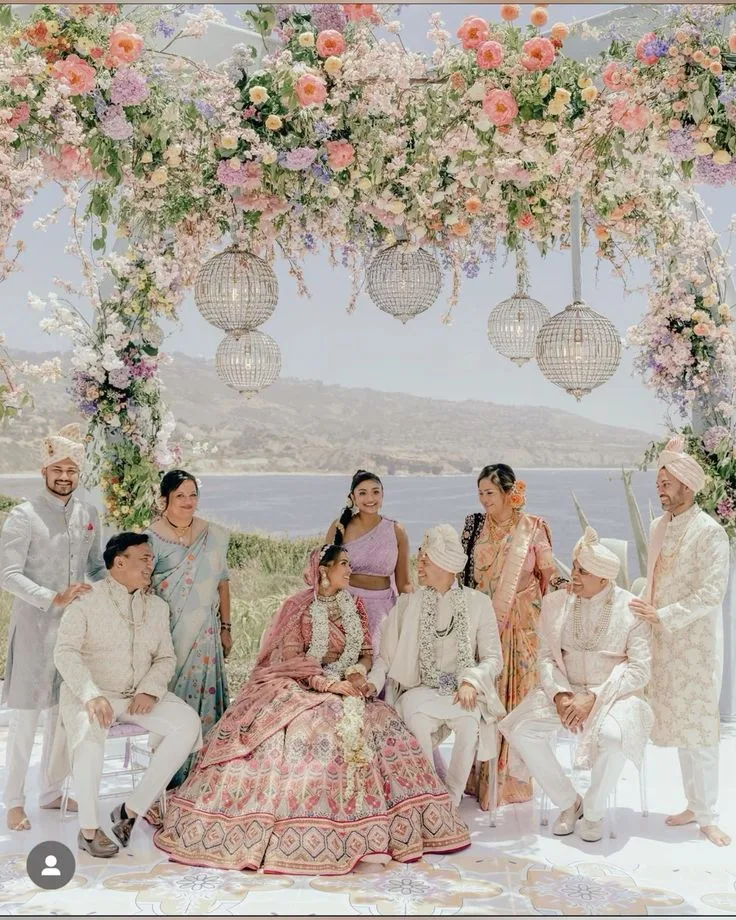A couple and their family gathered under a floral mandap by the sea