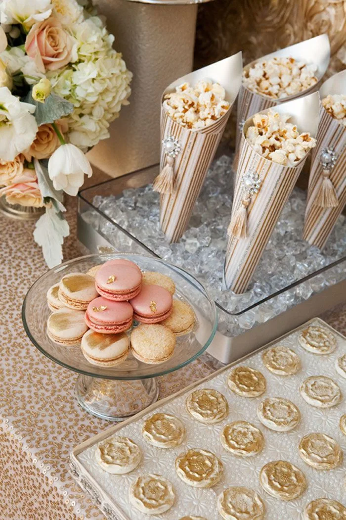A styled dessert table with popcorn cones, macarons and gold chocolates